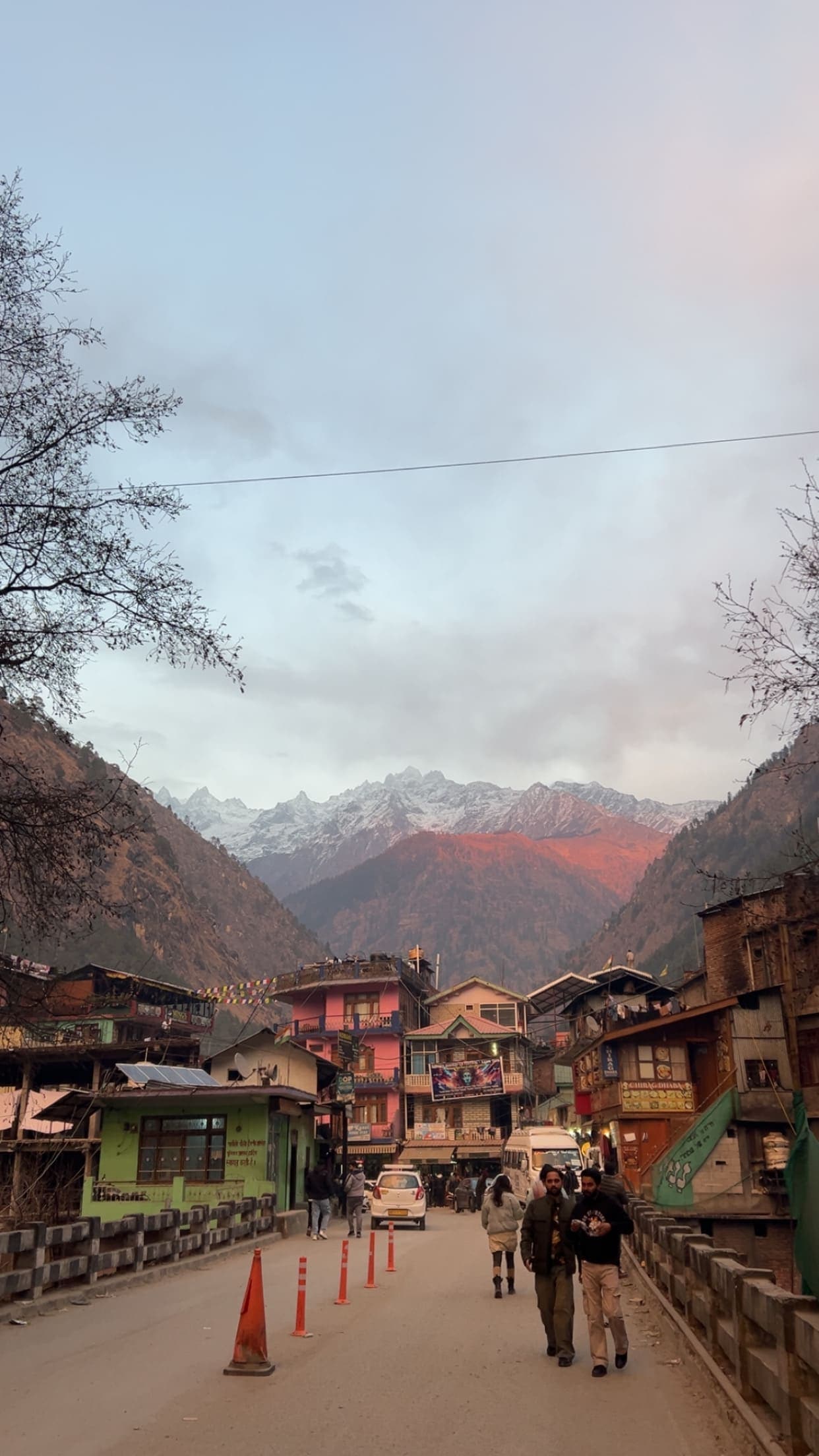 A cosy Himalayan mountain town street lined with cafes and dhabas at golden hour