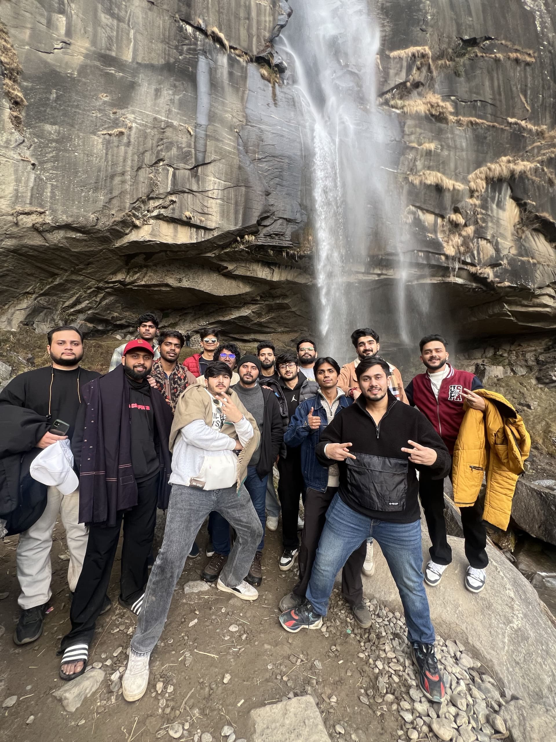 A lively TripoMusafir group posing together in front of a Himalayan waterfall