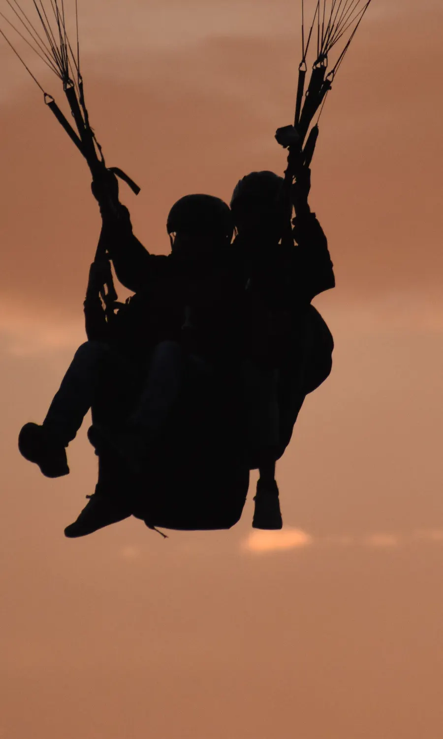 Close-up of a tandem paraglider arcing against the sunset sky