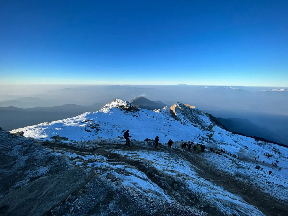 Trekkers on the summit ridge with the Himalayan range behind
