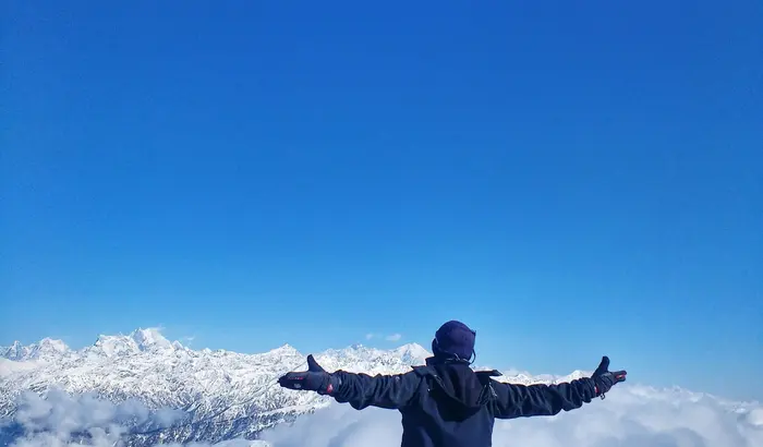A trekker celebrating above the clouds at the Kedarkantha summit