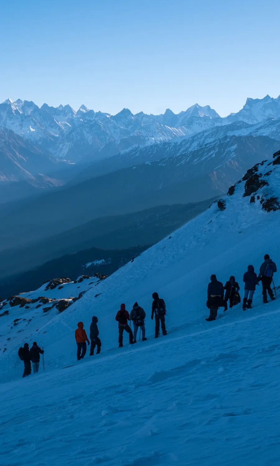 Trekkers with backpacks crossing the snow ridge near sunrise
