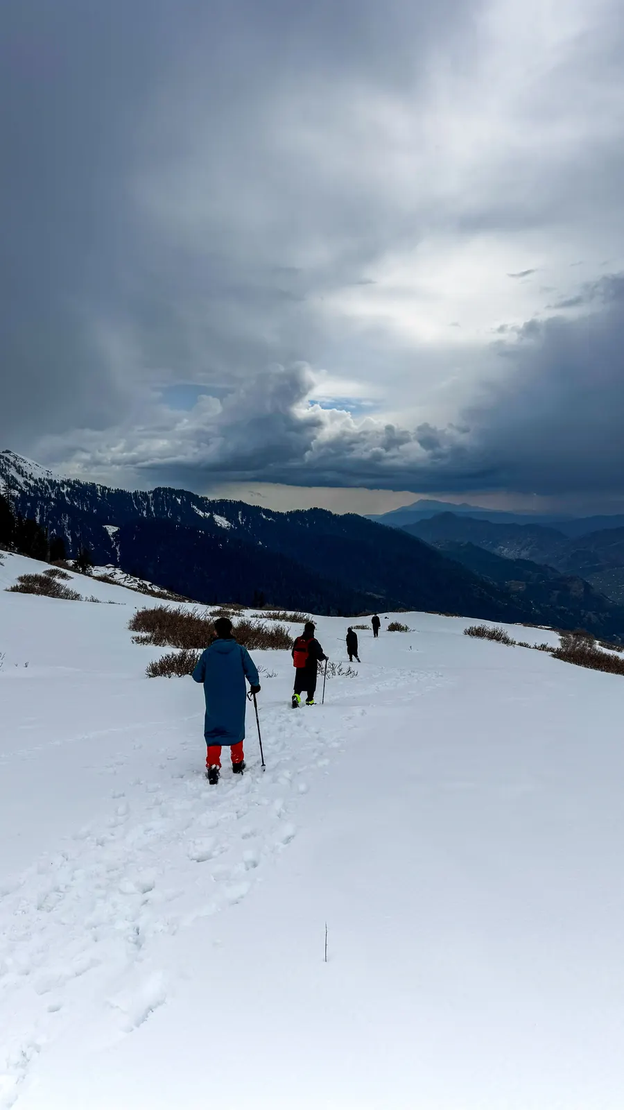 Trekkers climbing the snow ridge to Kedarkantha summit under a dramatic sky