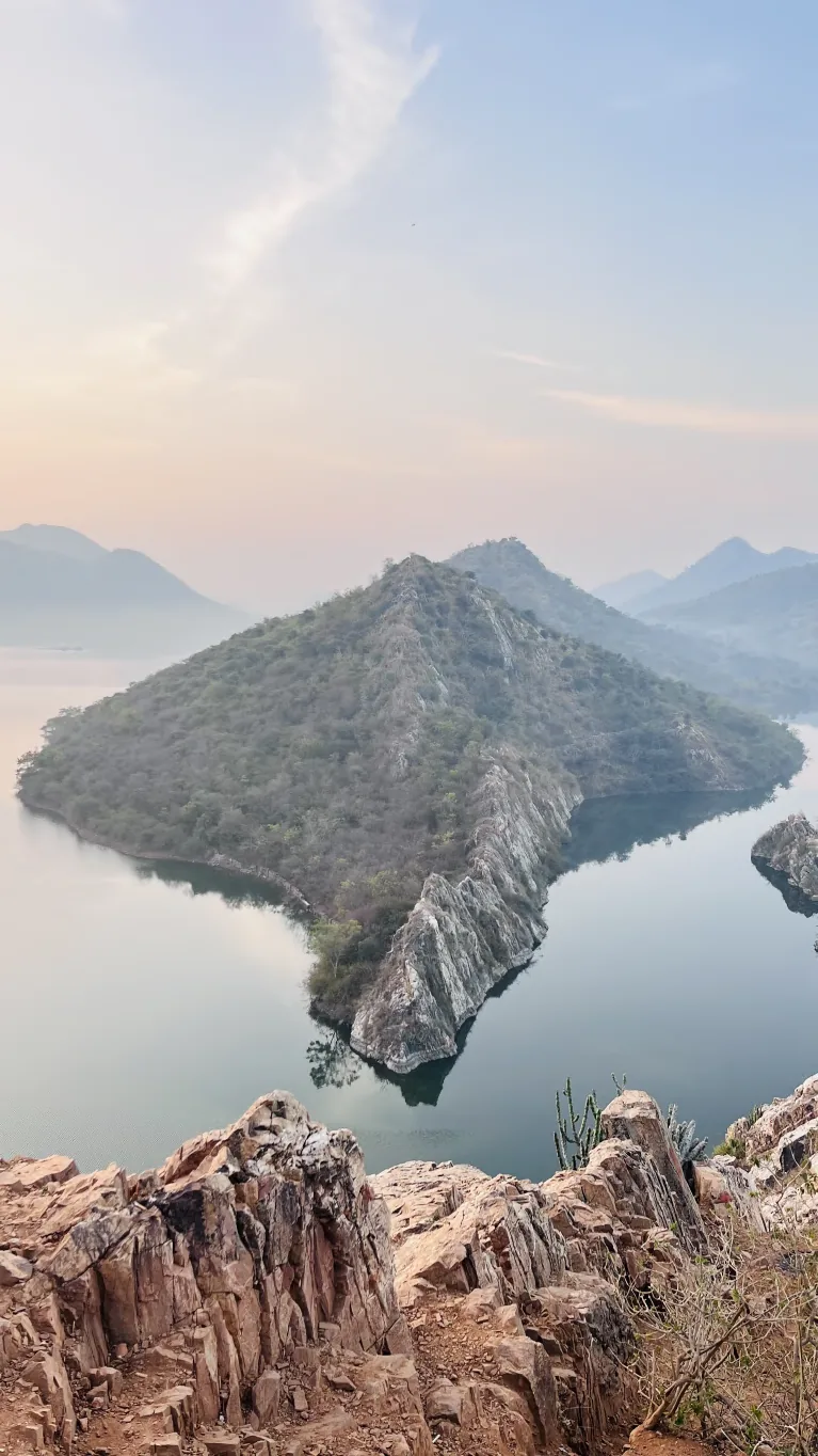 View over Bari Lake and a green rocky hill in the misty Aravalli range from Bahubali Hills near Udaipur